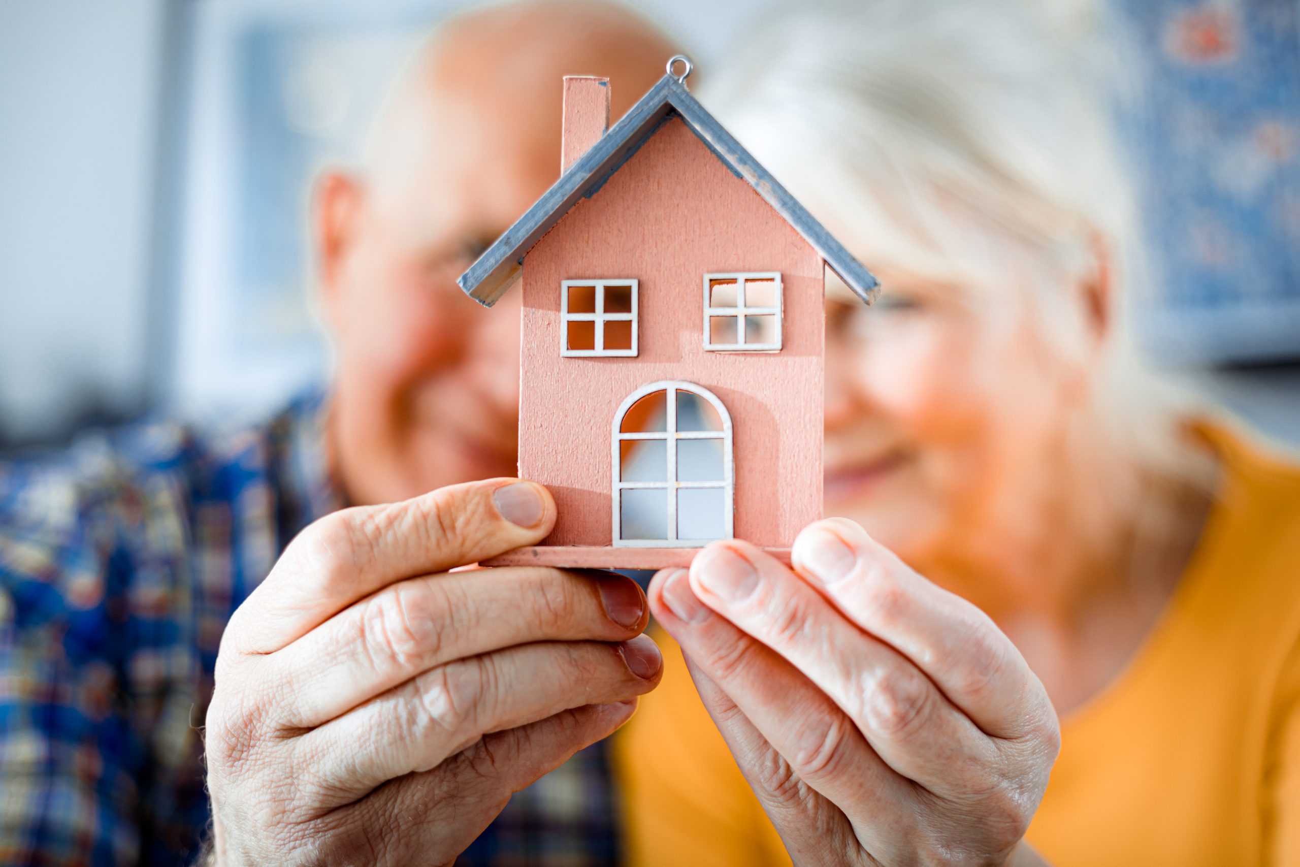 New house concept, happy senior couple holding small home model